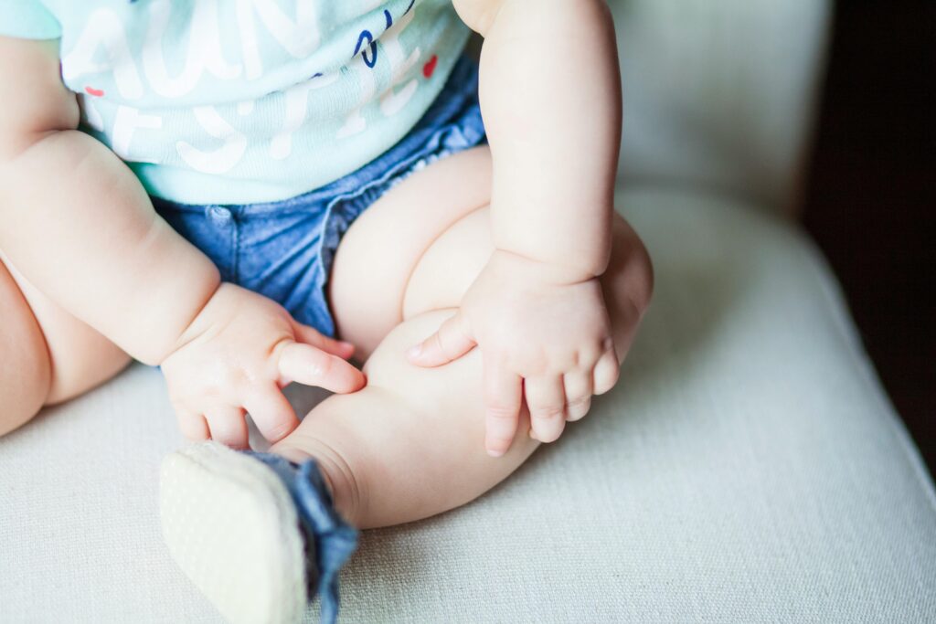 Adorable baby in denim shorts with focus on seated posture and hands.