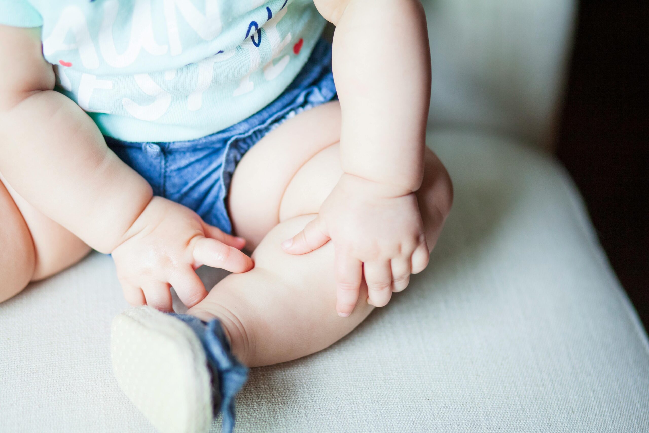 Adorable baby in denim shorts with focus on seated posture and hands.