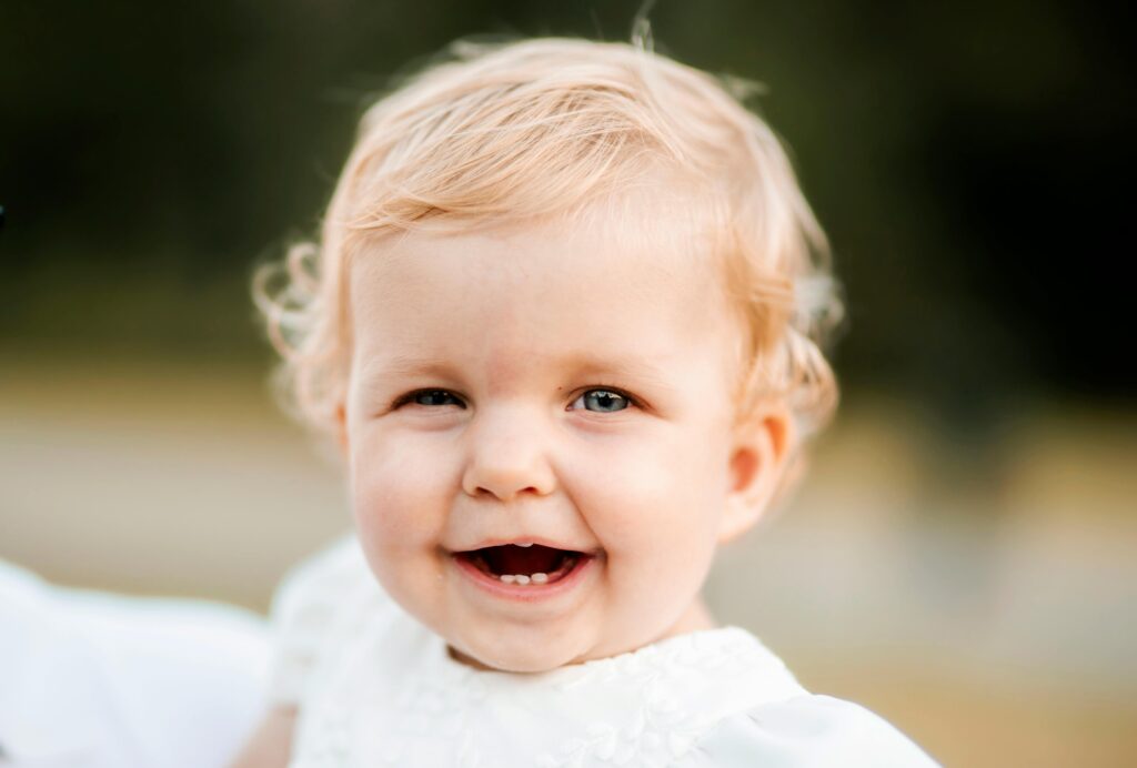 Close-up of a cute baby with blond hair smiling joyfully outdoors.