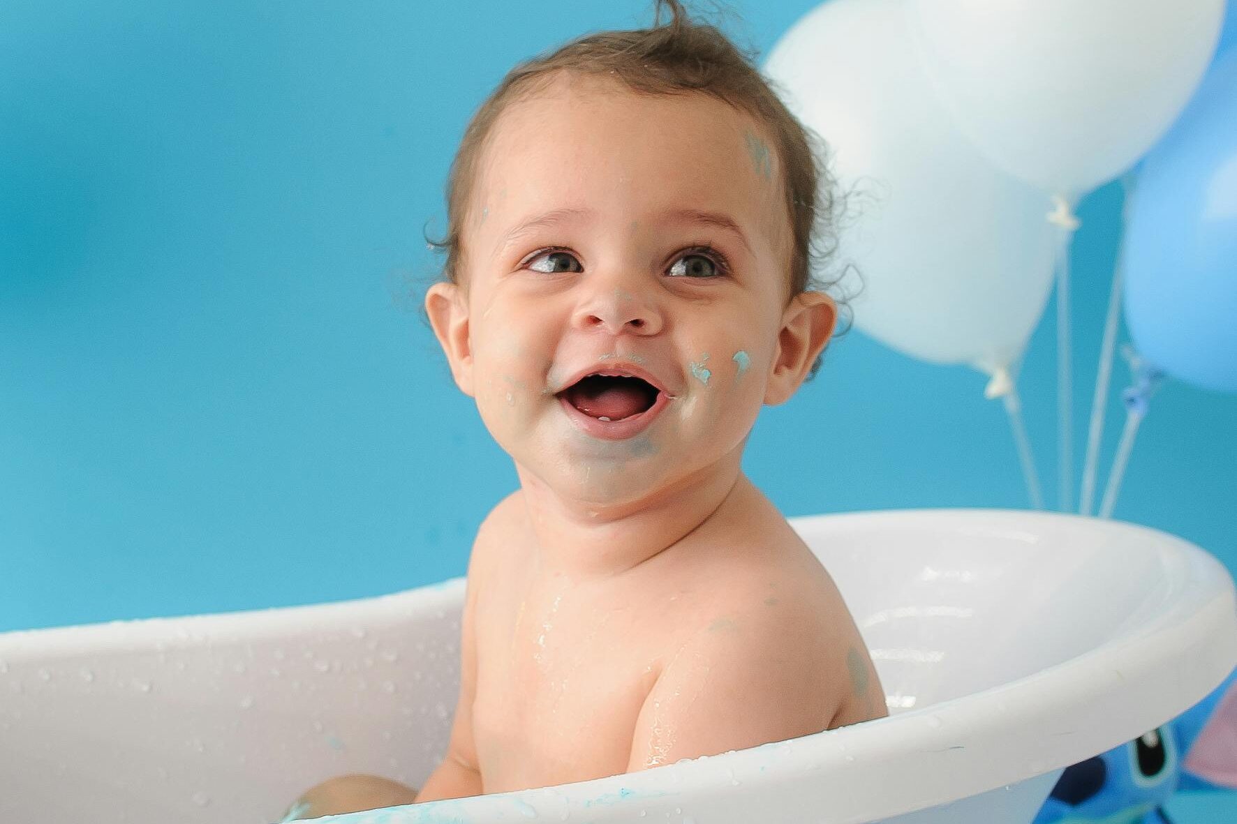 Adorable baby smiling in a bathtub with blue balloons, capturing joy and innocence.