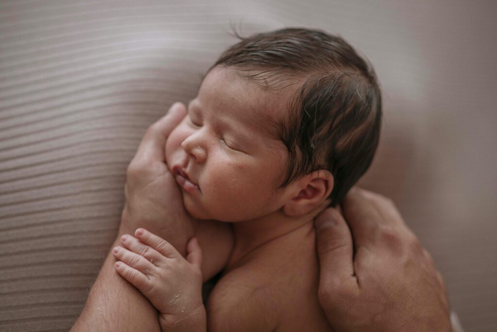 A serene image of a sleeping newborn cradled gently in a parent's hands. Captures the essence of warmth and care.