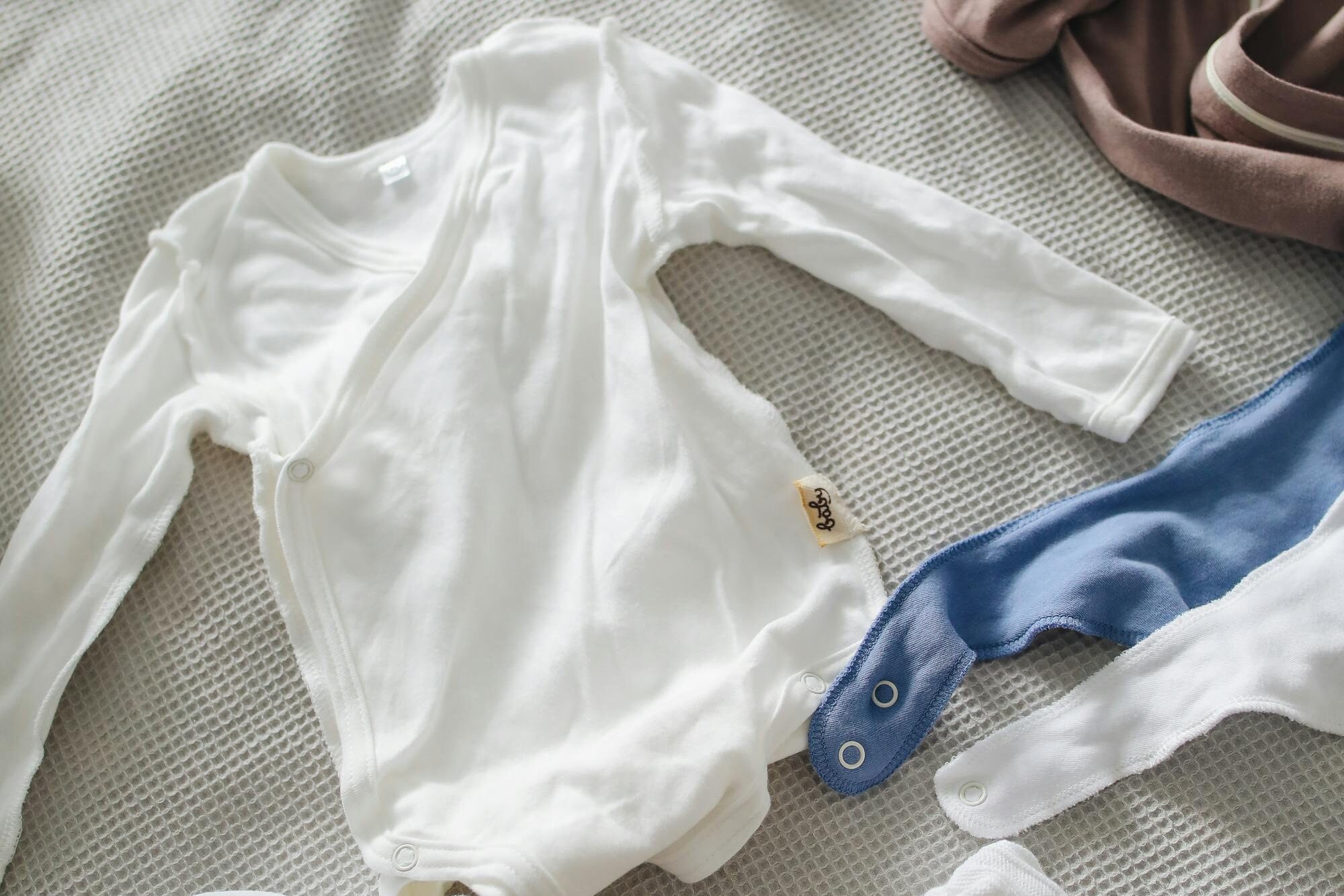 From above of cute cotton suits bibs socks and hats for little babies on gray bedspread on bed at home on daytime on gray