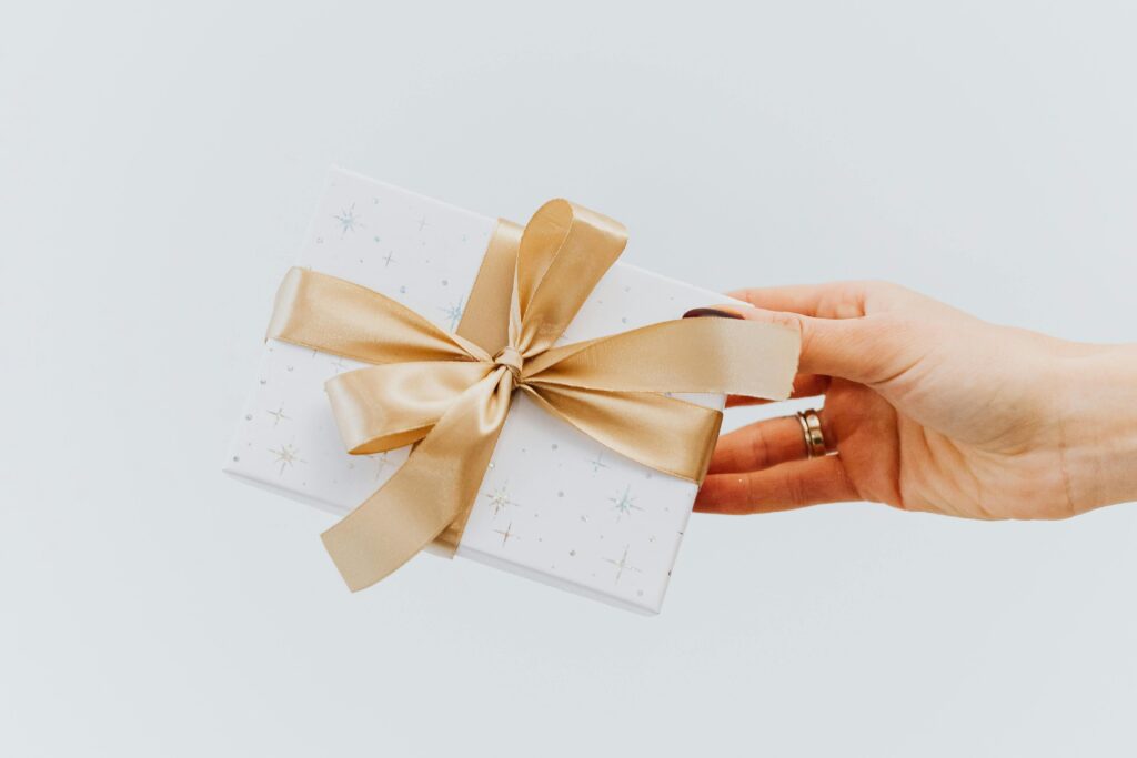 A hand holding an elegantly wrapped gift box with a gold ribbon on a white background.