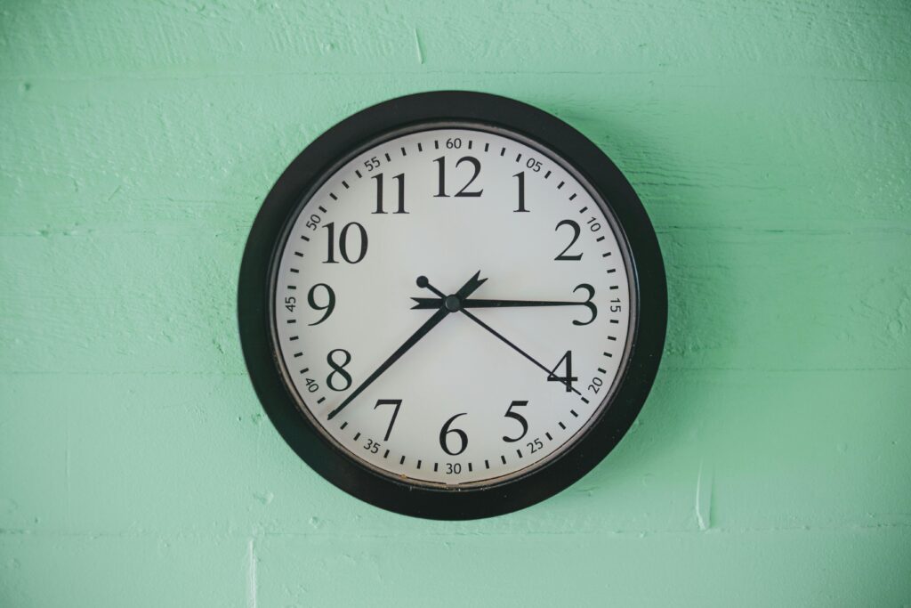 A classic round wall clock with black frame against a mint green wall, showing 7:23.